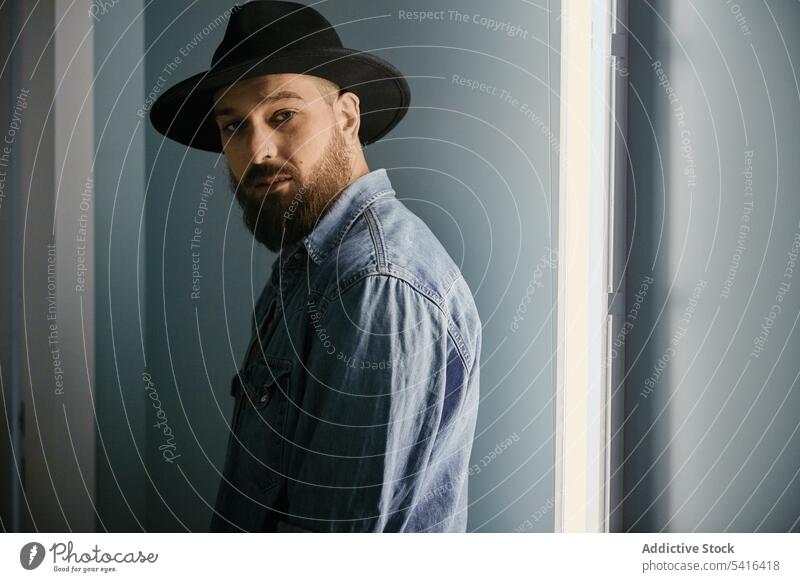 Gutaussehender Mann mit Hut schaut in die Kamera im Zimmer gutaussehend nachdenklich bärtig Erwachsener Model jung selbstbewusst männlich lässig Blick stylisch