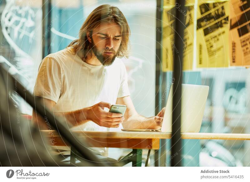 Hübscher Mann mit Telefon und Laptop gutaussehend Schnurrbart arbeiten Erwachsener Lifestyle Bartstoppel Frisur Fröhlichkeit bärtig Model jung selbstbewusst