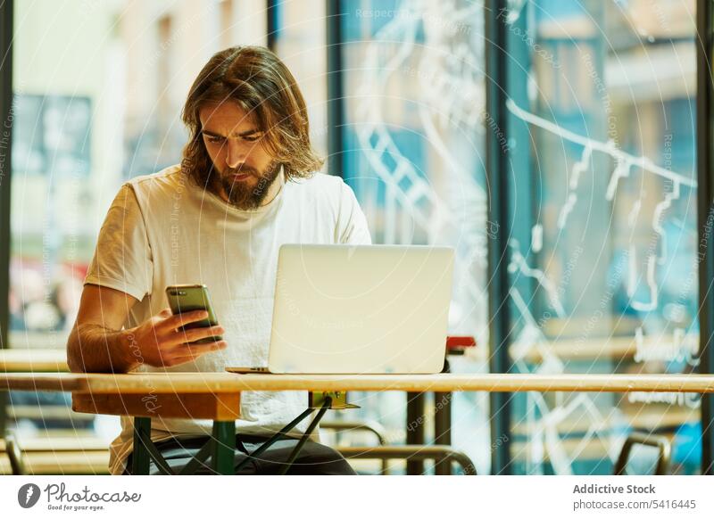 Hübscher Mann mit Telefon und Laptop gutaussehend Schnurrbart arbeiten Erwachsener Lifestyle Bartstoppel Frisur Fröhlichkeit bärtig Model jung selbstbewusst