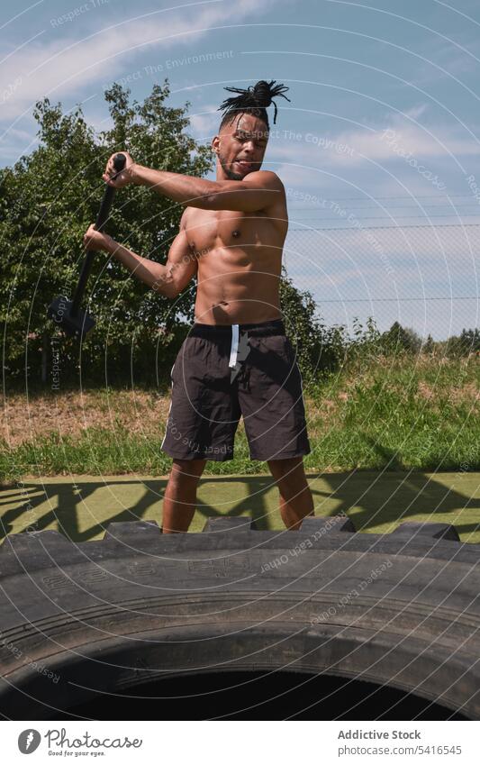 Muskulöser schwarzer Mann hämmert Reifen in einem Fitnessstudio im Freien Hammer Übung schlagend ohne Hemd muskulös anstrengen Training Athlet männlich Sport