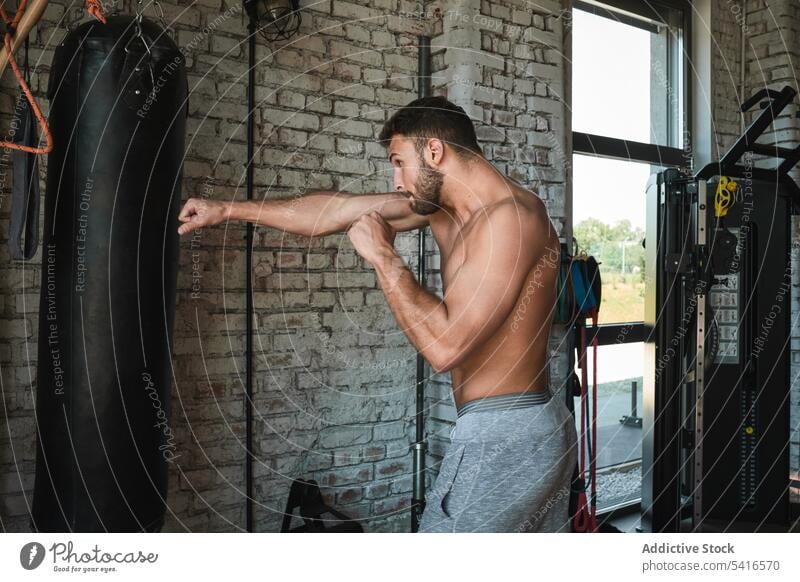 Mann boxt im Fitnessstudio Boxsport Tasche Stanzen Training ohne Hemd Sport muskulös männlich jung Athlet Stärke Kraft Kämpfer passen Übung Tatkraft Typ