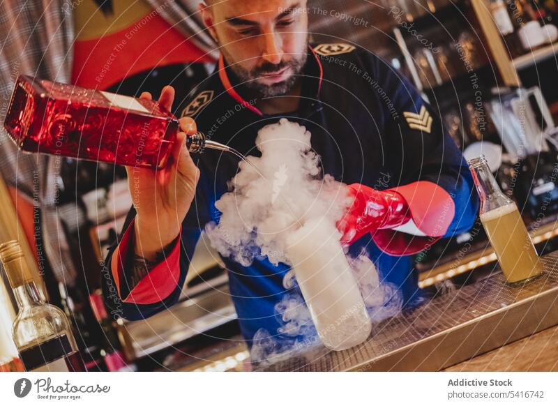 Barkeeper mit roten Handschuhen bei der Zubereitung eines rauchenden Cocktails Alkohol Gießen Nachtclub mitreißend vorbereitend Mischen Flasche Rauchen Barmann