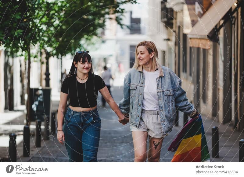 Lesbisches Paar mit LGBT-Flagge auf der Straße lesbisch Fahne lgbt laufen Glück winkend Großstadt jung Zusammensein Frauen lässig Homosexualität Stolz