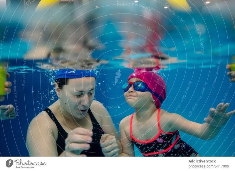 Fröhliches Mädchen beim Unterwasserschwimmen im Pool mit Mutter Schwimmsport Wasser Park aufgeregt Spaß Wochenende Zusammensein Vergnügen Frau Kind Schutzbrille