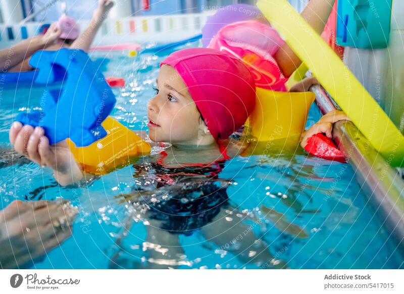 Ethnisches Mädchen mit Schwimmflügeln im Schwimmbad Spielen Wasser Park Schwimmsport Pool aufblasbar Flügel ethnisch Spielzeug Spaß Kind Freude Glück wenig