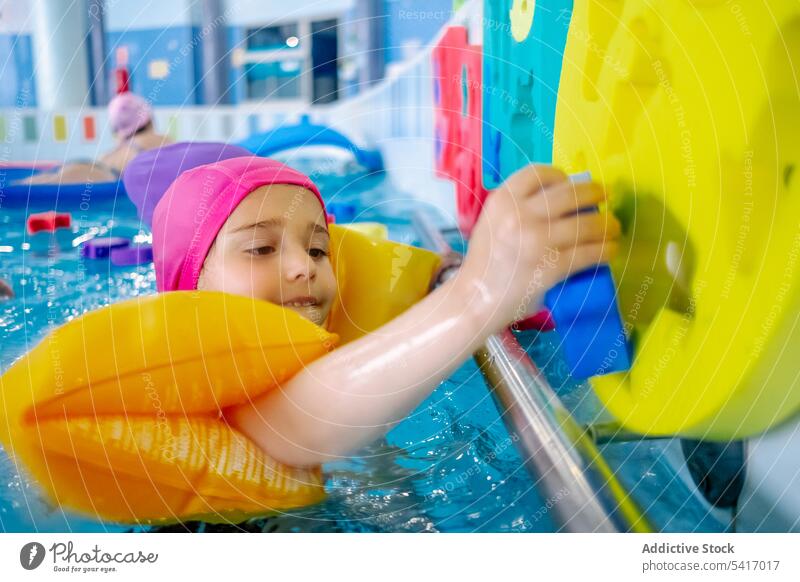 Ethnisches Mädchen mit Schwimmflügeln im Schwimmbad Spielen Wasser Park Schwimmsport Pool aufblasbar Flügel ethnisch Spielzeug Spaß Kind Freude Glück wenig