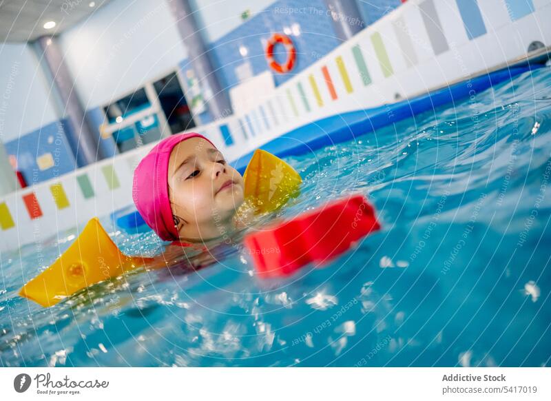 Ethnisches Mädchen mit Schwimmflügeln im Schwimmbad Spielen Wasser Park Schwimmsport Pool aufblasbar Flügel ethnisch Spielzeug Spaß Kind Freude Glück wenig