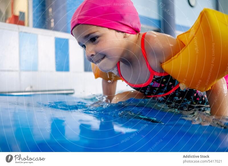 Ethnisches Mädchen mit Schwimmflügeln im Schwimmbad Spielen Wasser Park Schwimmsport Pool aufblasbar Flügel ethnisch Spielzeug Spaß Kind Freude Glück wenig