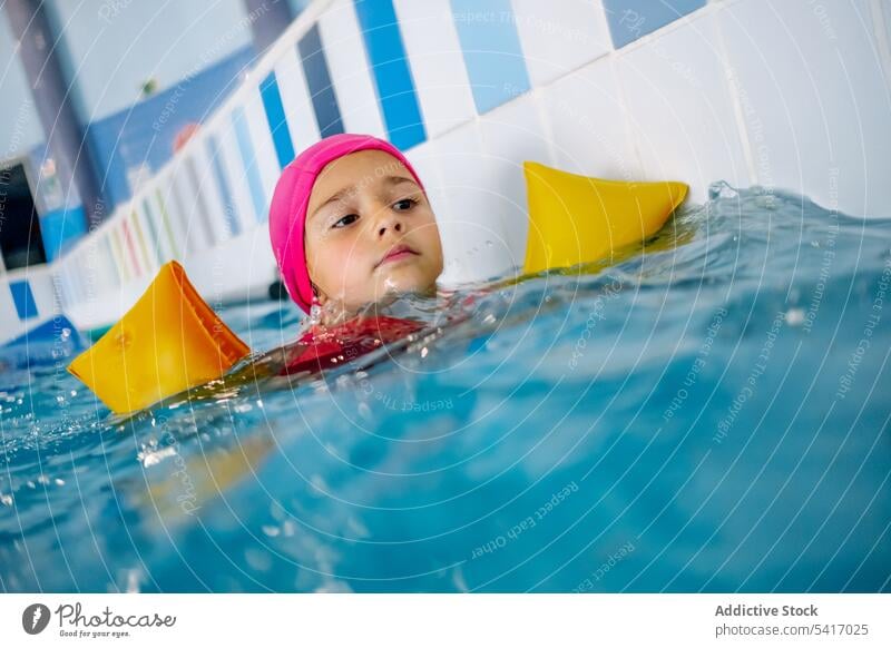 Ethnisches Mädchen mit Schwimmflügeln im Schwimmbad Spielen Wasser Park Schwimmsport Pool aufblasbar Flügel ethnisch Spielzeug Spaß Kind Freude Glück wenig