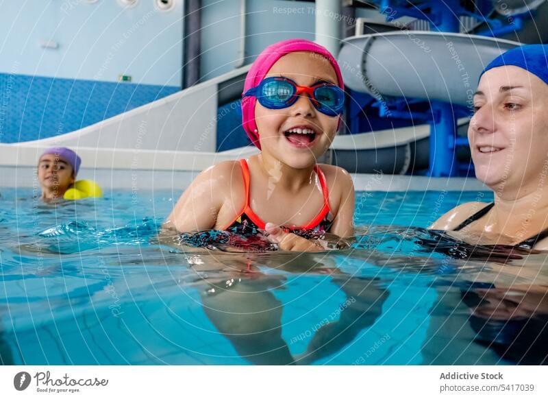 Fröhliches Mädchen schwimmt mit Mutter im Pool Schwimmsport Wasser Park aufgeregt Spaß Wochenende Zusammensein Vergnügen Frau Kind Schutzbrille Hut heiter Glück