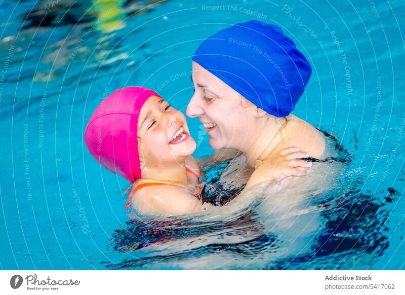 Fröhliches Mädchen schwimmt mit Mutter im Pool Schwimmsport Wasser Park aufgeregt Spaß Wochenende Zusammensein Vergnügen Frau Kind Schutzbrille Hut heiter Glück