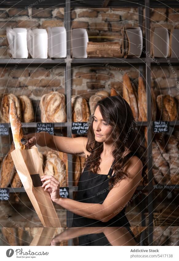 Junge Frau verkauft Baguette Bäckerei Brot Französisch traditionell frisch Lebensmittel Beruf Job jung Person schön attraktiv hübsch brünett Stehen arbeiten