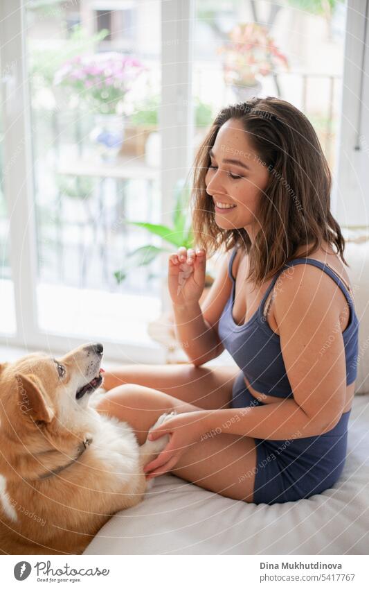 Millennial kaukasische Frau zu Hause mit Corgi Hund. Hundetrainer. Lustige gemütliches Bild der Frau mit Welpe in der Wohnung. Brunette lächelnd mit welsh Corgi Pembroke Hund sitzt auf Couch.