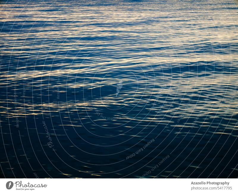 Dunkelblaue Meerwasseroberfläche mit schwachen Sonnenlichtreflexen. abstrakt aqua Hintergrund schön hell Windstille Ruhe Sauberkeit Abenddämmerung gold golden