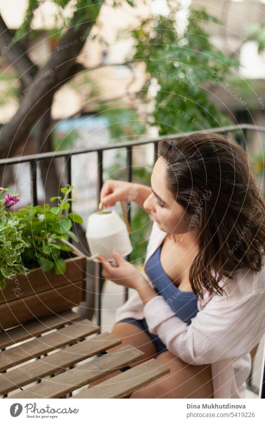 Schöne Frau bewässert grüne Pflanzen auf dem Balkon Großaufnahme. Glückliche Brünette lächelnd. Pflanzen und Blumen Gartenarbeit Hobby. Urbane Dschungel Millennial Hause Interieur Wohnung.