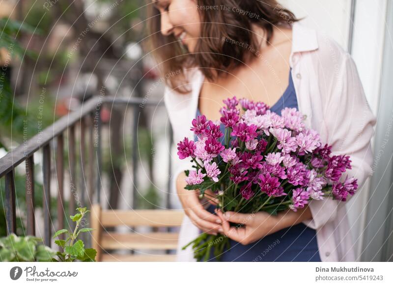 Schöne Frau mit Blumenstrauß auf dem Balkon Großaufnahme. Glückliche Brünette lächelnd. Pflanzen und Blumen Gartenarbeit Hobby. Balkonpflanze Balkondekoration