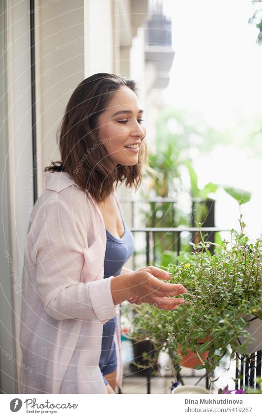 Schöne Frau lächelnd, die Pflege von Grünpflanzen auf dem Balkon Nahaufnahme. Glückliche Brünette lächelnd. Pflanzen und Blumen Gartenarbeit Hobby. Urbane Dschungel Millennial Hause Interieur Wohnung.