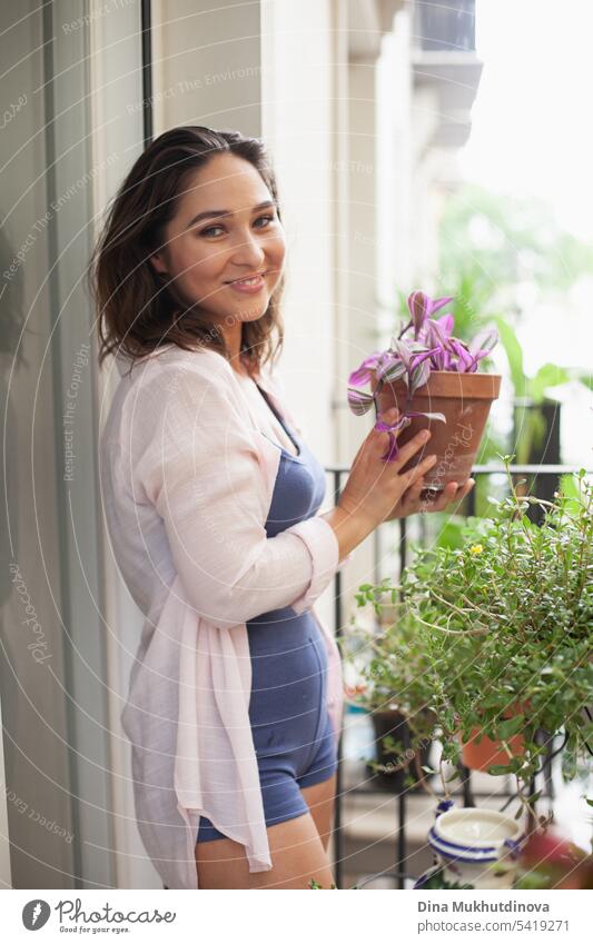 Schöne Frau mit Zimmerpflanze auf dem Balkon. Glückliche Brünette lächelnd. Pflanzen und Blumen Gartenarbeit Hobby. Balkonpflanze Balkondekoration Sommer