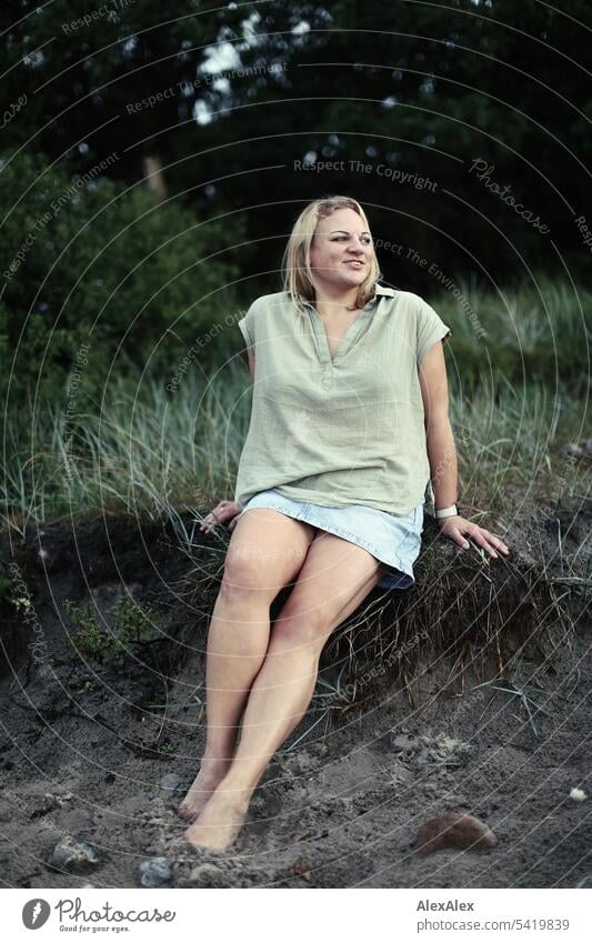 Portrait einer schönen, blonden Frau auf der Dünenkante sitzt und sich freut langhaarig blonde Haare Freude Lächeln Strand Sand Dünengras Schönheit entspannt