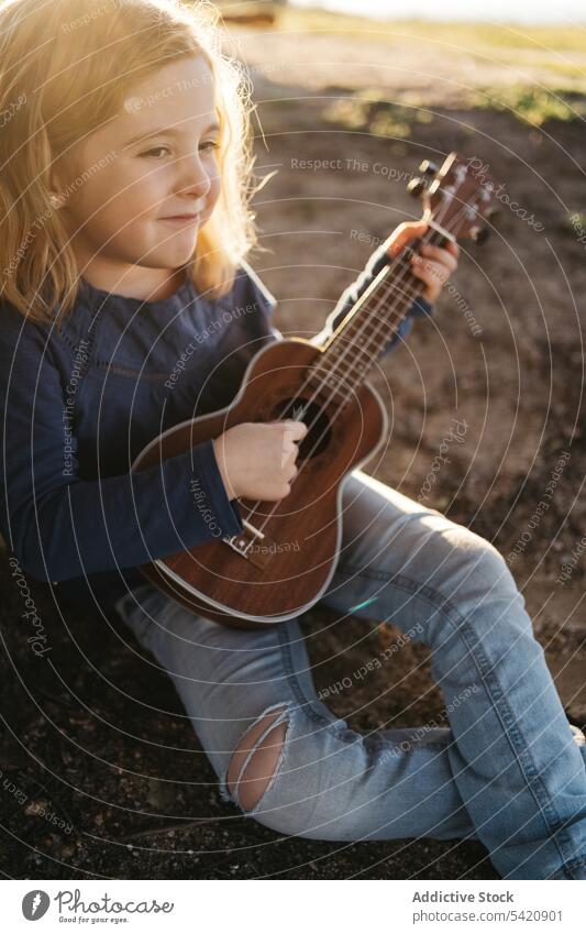 Kleines Mädchen sitzt unter einem Baum und spielt Ukulele Kind spielen Musik Gitarre Natur Sommer ernst wenig Instrument Klang Gesang Melodie sitzen Kofferraum