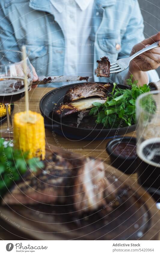 Person isst gegrilltes Fleisch in einem Restaurant Grillrost Mais Steak essen Kraut grün Braten geschmackvoll Knochen Barbecue rustikal hölzern Lebensmittel