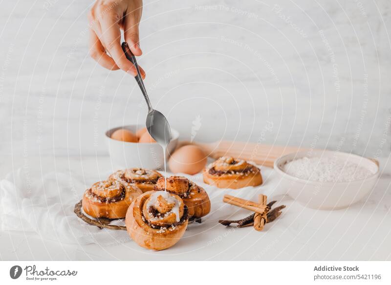 Koch gießt Zuckerguss auf frisch gebackene Zimtschnecken rollen Brötchen Zuckerguß eingießen Top süß Bäckerei bestäuben Lebensmittel vorbereiten natürlich