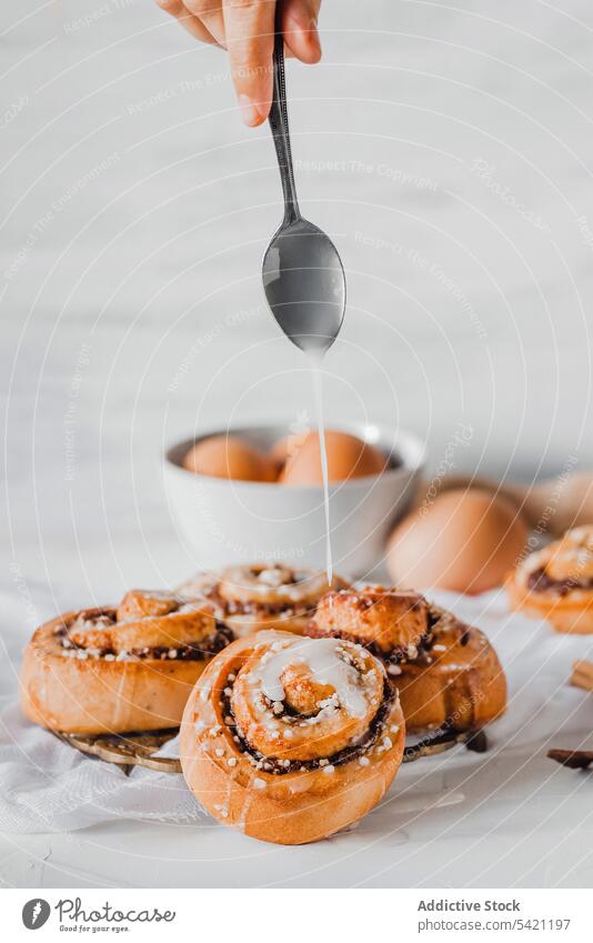 Koch gießt Zuckerguss auf frisch gebackene Zimtschnecken rollen Brötchen Zuckerguß eingießen Top süß Bäckerei bestäuben Lebensmittel vorbereiten natürlich