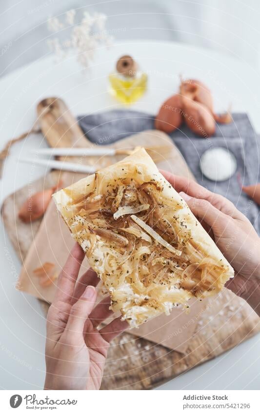 Person, die ein Stück Blätterteig mit Zwiebeln und Frischkäse nimmt Gebäck Spielfigur Bestandteil Schneidebrett Sahne Käse Hauch rustikal Tradition Mahlzeit