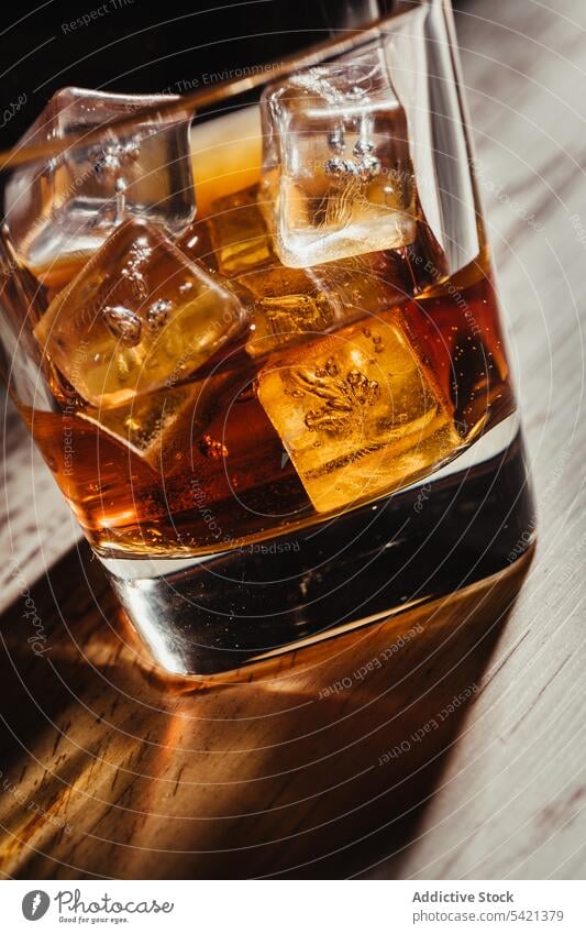 Glas Scotch in Strahlen auf alten rustikalen Tisch in der Dunkelheit Whiskey Bourbon Alkohol Getränk Eis trinken liquide Schnaps Cognac Weinbrand durchsichtig