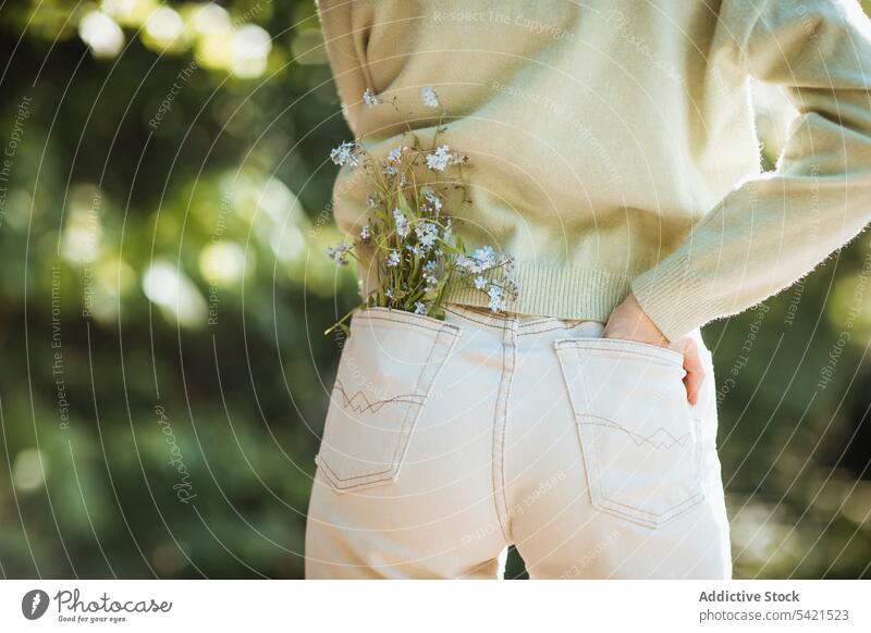 Unerkanntes Teenager-Mädchen mit Blumen in der Jeanstasche Jeanshose Tasche Angebot Sommer Wildblume Park sanft Natur stehen Blütezeit Stil Flora Saison