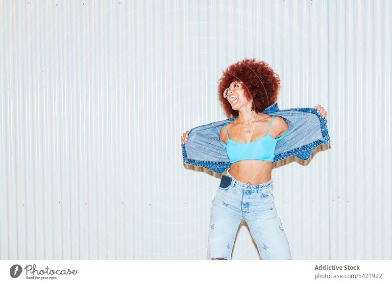 Glückliche Frau in Jeans-Outfit in der Nähe der Wand Afro-Look Stil Mode trendy Bekleidung Spaß haben sorgenfrei Stimmung Vorschein Straße Frisur Sonnenbrille