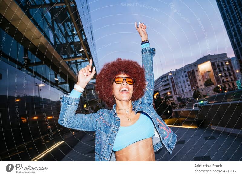 Stilvolle Frau hat Spaß auf dunkler Straße Afro-Look Mode Outfit Gebäude urban Abend Spaß haben Glück Bekleidung positiv Lächeln Arme hochgezogen sorgenfrei