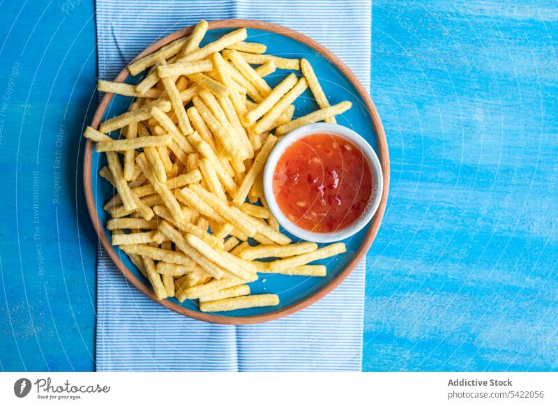 Keramikteller mit Pommes frites und Schale mit süß-saurer Soße Französisch Fries sauer Saucen Schalen & Schüsseln Oberfläche Serviette blau Stoff hoher Winkel