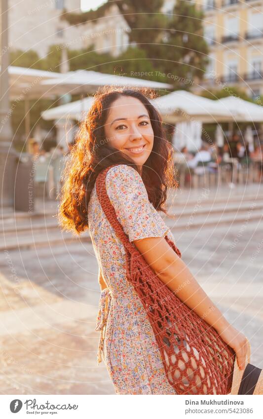 schöne Brünette Frau Tourist in europäischen Stadt lächelnd bei Sonnenuntergang, zu Fuß auf der Straße in der Nähe von Café oder Restaurant Terrasse. Weibliche Alleinreisende schaut in die Kamera in Valencia, Spanien.