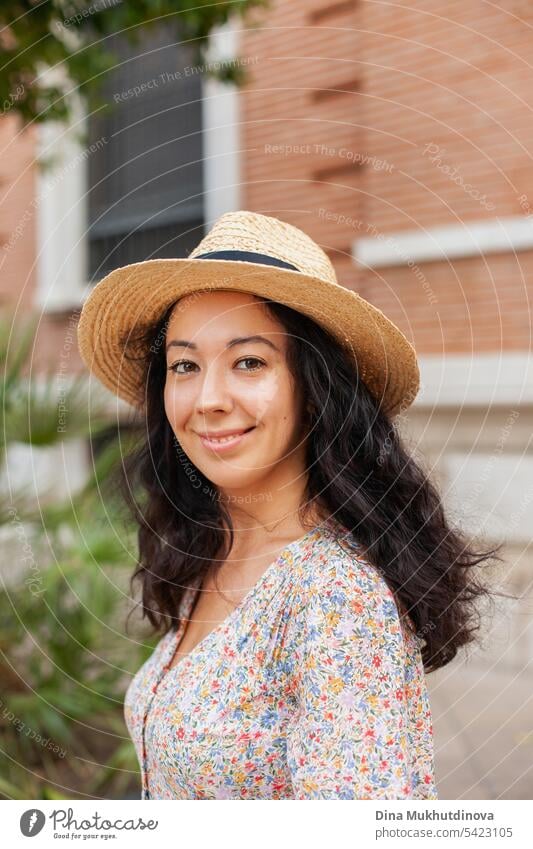 schöne brünette Frau mit Hut, lächelnd, in einer europäischen Stadt. Weiblicher Alleinreisender, der in Spanien oder Italien im Sommerurlaub in die Kamera schaut