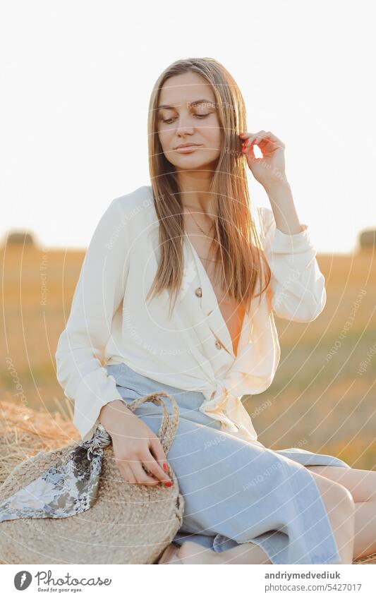 Schönes Porträt einer jungen Frau während des Sonnenuntergangs mit warmen gelben Sonnenstrahlen auf ihr Gesicht mit Strohballen auf dem Hintergrund ländlich