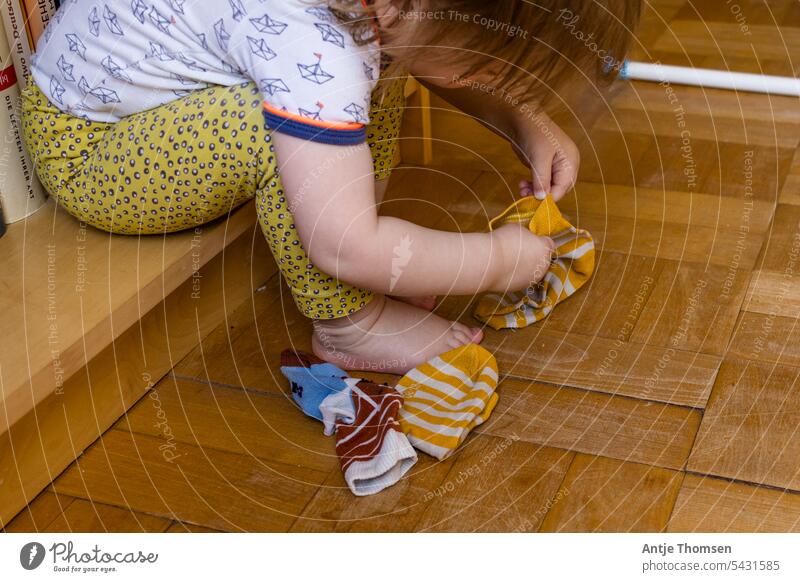 Kleinkind sitzt in einem Bücherregal und versucht sich Socken anzuziehen Socken anziehen montessori sitzen Füße dokumentarisch Alltagsfotografie Kind