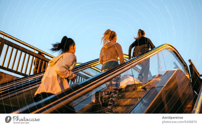 Frauen Freunde Ausbildung laufen auf Rolltreppe in der Stadt bei Sonnenuntergang unkenntlich Menschengruppe Läufer Team Training rennen Mechaniker Treppe