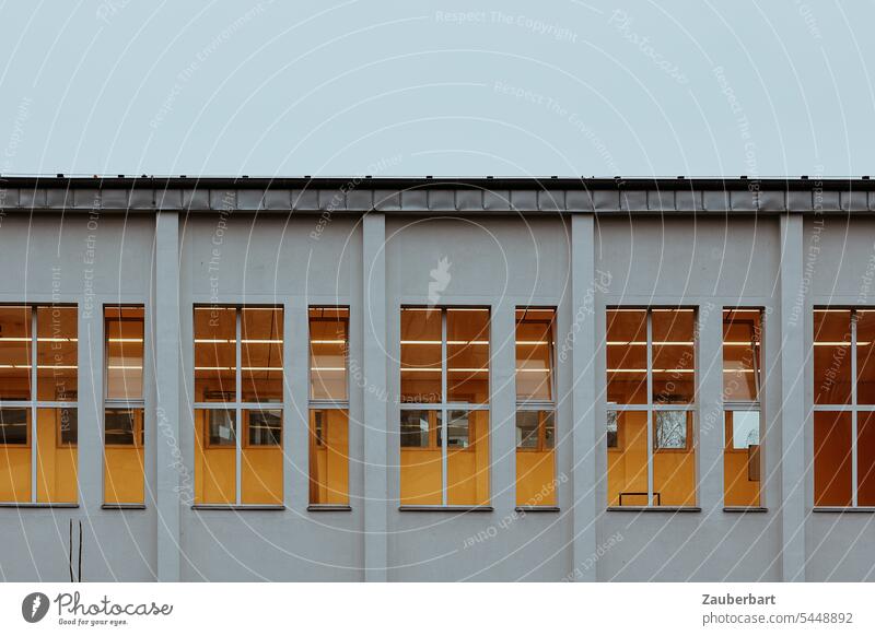 Sporthalle, Gebäude mit großen Fenstern, beleuchtet mit gelbem Licht, in der Abenddämmerung Fassade Abendlicht symmetrisch geordnet ordentlich Architektur Haus