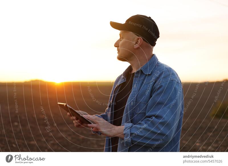 Intelligente Landtechnik und Landwirtschaft. Ein Landwirt benutzt ein digitales Tablet auf einem Feld mit gepflügtem Boden bei Sonnenuntergang. Überprüfung und Kontrolle der Bodenqualität, der Bereitschaft zur Aussaat von Pflanzen und zum Anbau von Gemüse