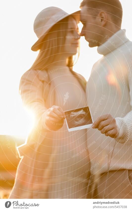 Unerkannt von einer schwangeren Frau mit ihrem Mann halten ein Ultraschall-Scan-Foto des ungeborenen Kindes im Freien auf die Natur in Sonnenlicht. Glückliche Mutterschaft und Elternschaft Konzept