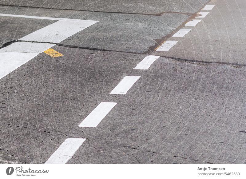 Straßenmarkierungen an einer Ampel auf kaputtem, teilweise geflicktem Asphalt Straßenübergang Fahrbahnmarkierung weiße streifen gelb farbklecks Orientierung