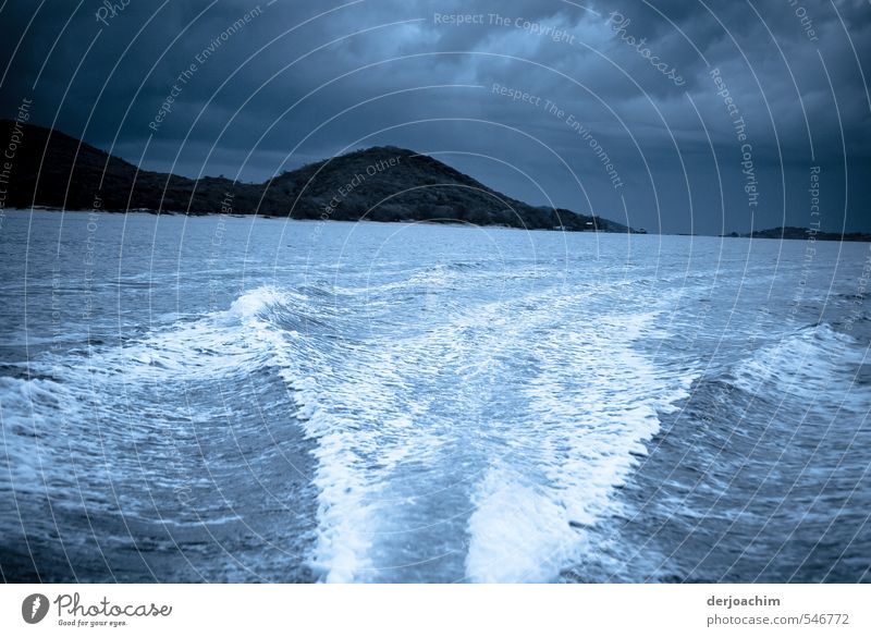 Dunkle Wolken im Hintergrund . Mit schneller Fahrt fährt das Motorboot von der Insel weg Man sieht eine starke Bugwelle auf dem Wasser. Gewitterstimmung Natur