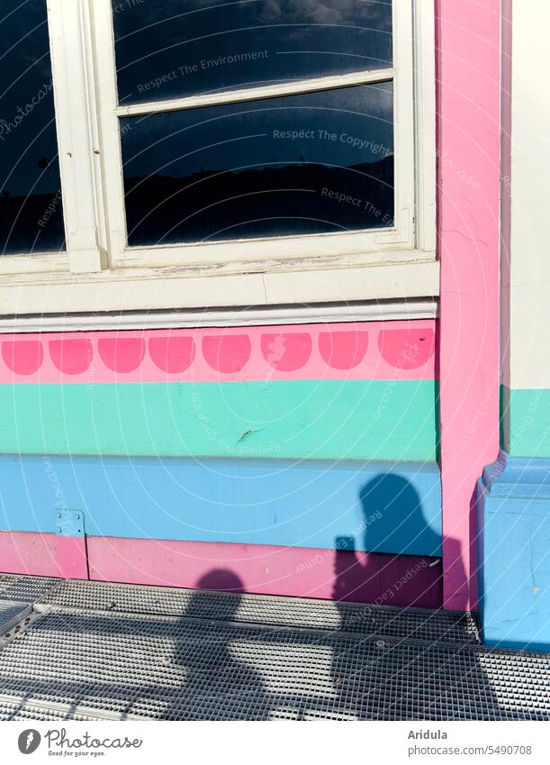 Schatten zweier Menschen auf einer bunten Hausfassade mit Fenster, eine Person hält ein Handy in der Hand Personen Umriss Schattenwurf Silhouette