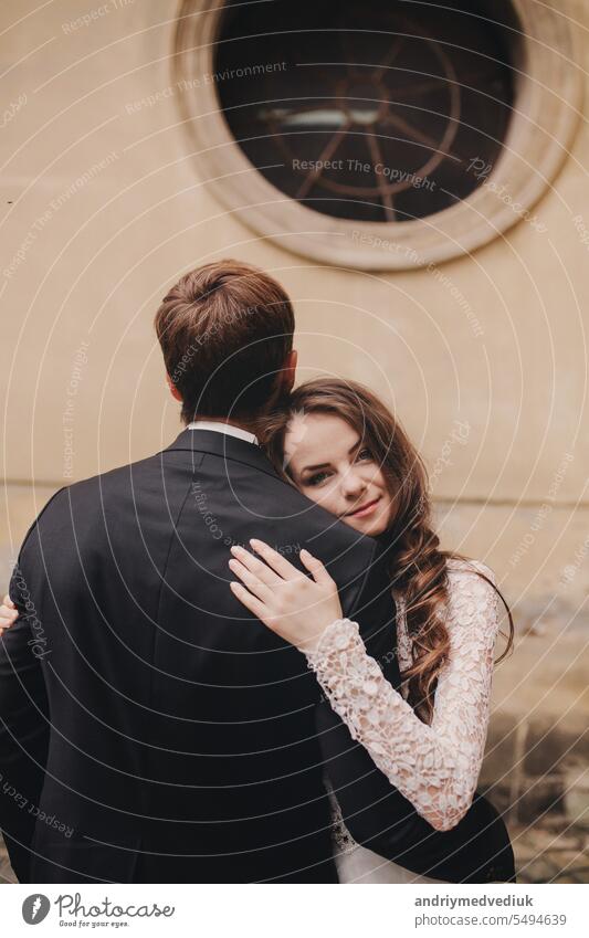 Stilvolle Braut und Bräutigam sanft umarmt in europäischen Stadt Straße. Gorgeous Hochzeit Paar von Jungvermählten umarmt in der Nähe von alten Gebäude. Romantischer Moment. Hochzeitstag