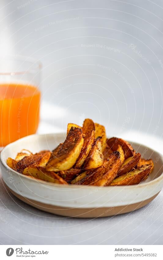 Gebratene Kartoffel mit Paprikagewürz, serviert auf einem Keramikteller neben Orangensaft gebraten Gewürz orange Saft Lebensmittel trinken Glas Tisch Teller