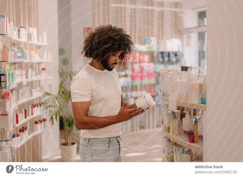 Schwarzer Mann mit Afrofrisur liest Etikett auf Flasche in Apotheke lesen kennzeichnen Bestandteil Medizin Drogerie kaufen Kunde Medikament Paket