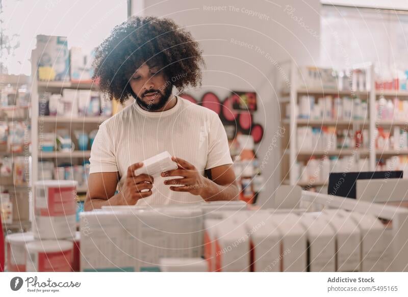 Afroamerikanischer Mann mit Afrohaar liest in der Apotheke das Etikett eines verschriebenen Medikaments lesen kaufen Information Medizin Kunde Verschreibung