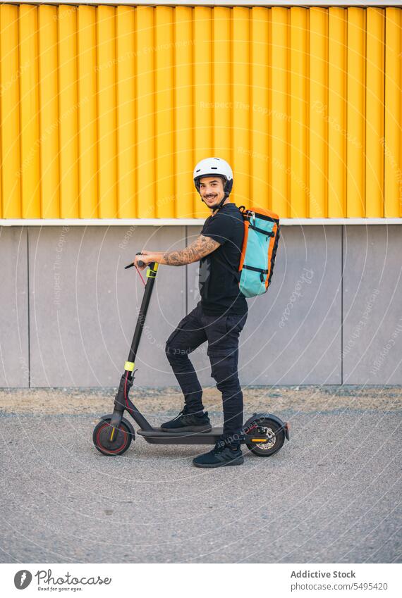 Kurierdienstmitarbeiter mit Elektroroller auf der Straße schaut in die Kamera Auslieferer Kickroller elektrisch Mitfahrgelegenheit Verkehr Dienst Arbeiter