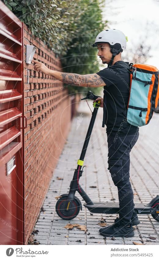 Kuriermann klingelt an der Tür eines Hauses in der Nachbarschaft Auslieferer elektrisch Kickroller Verkehr Dienst Ring Klingel Gate Versand modern Schutzhelm